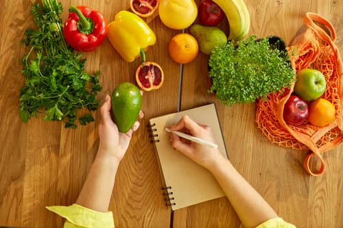 Frau plant wöchentliche Mahlzeiten mit einem Essensplaner-Notizbuch