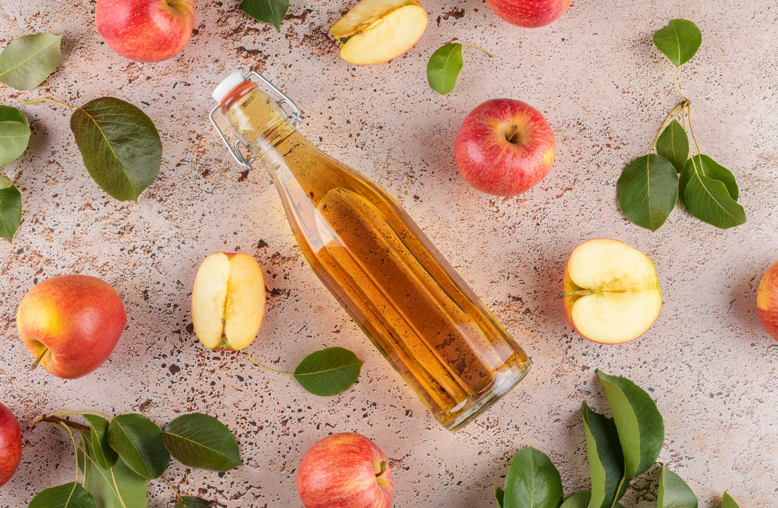 Apfelessig in einer Glasflasche neben Äpfeln auf einem grauen Untergrund