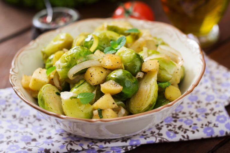 Eine Schüssel Rosenkohl mit Äpfeln und Haselnüssen, garniert mit frischem Parmesan, auf einer Serviette mit Blumenmotiv.